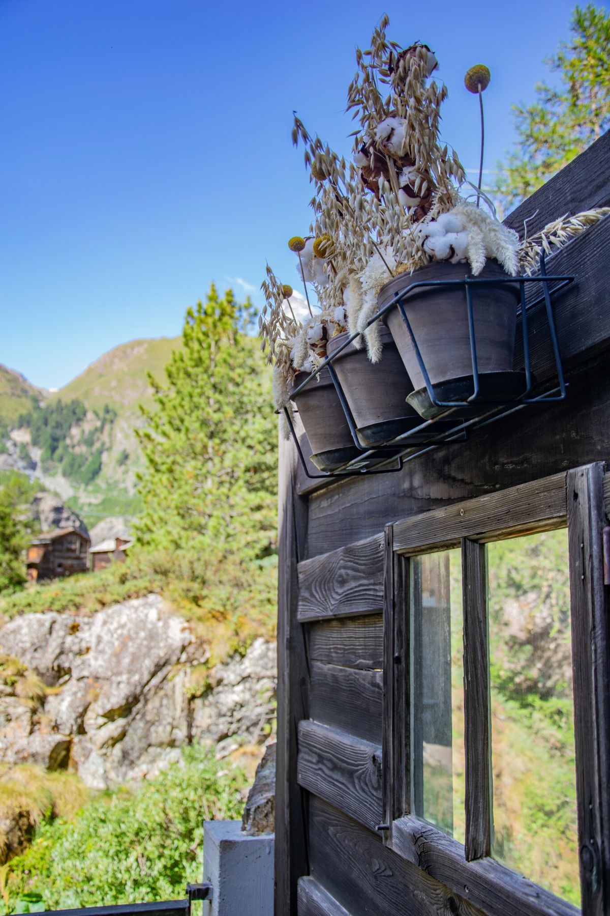 Holzfassade des Restaurant Alm mit Fenster, Blumen und Wiesen am Hang